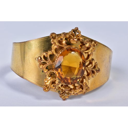 151 - A VICTORIAN GILT METAL BANGLE, the foliate scroll mount set with a central facet cut citrine, taperi... 