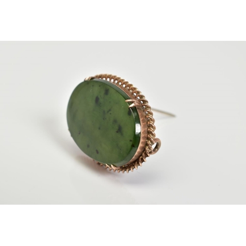 61 - A BROOCH, of oval design set with a nephrite panel within a four claw setting and rope twist surroun... 