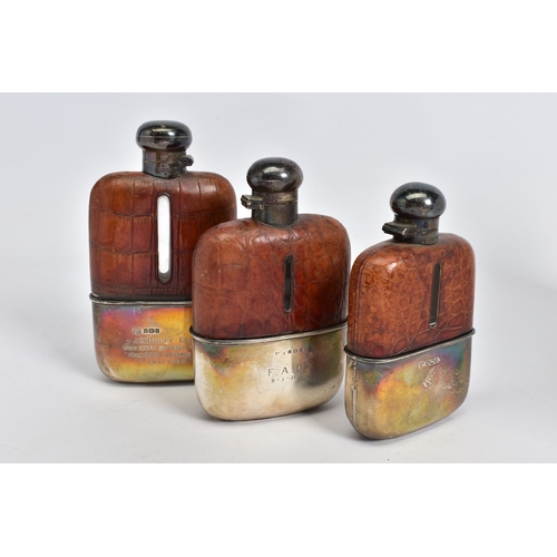 181 - A SET OF THREE GRADUATED SILVER AND CROCODILE SKIN GLASS HIP FLASKS with quarter turn caps