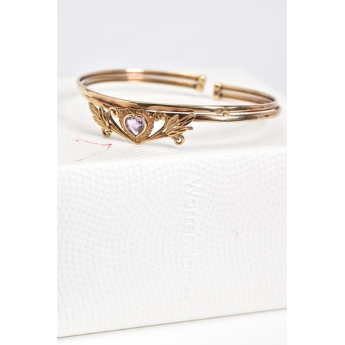 19 - AN AMETHYST SET BANGLE, set with a central heart shaped amethyst within a floral detail panel, to th... 