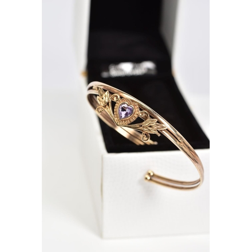 19 - AN AMETHYST SET BANGLE, set with a central heart shaped amethyst within a floral detail panel, to th... 