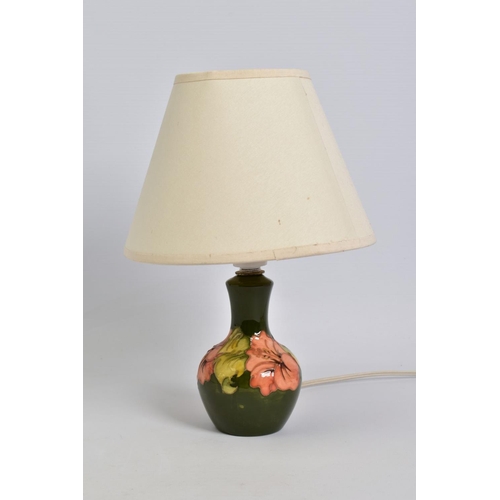 551 - A MOORCROFT POTTERY TABLE LAMP, of bulbous form, green ground with coral hibiscus, cream fabric shad... 