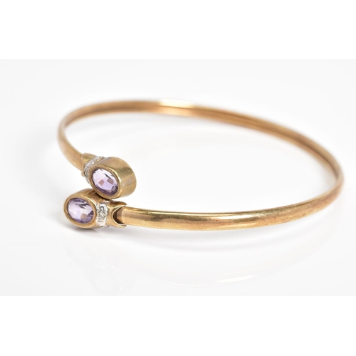 22 - A 9CT GOLD CROSSOVER BANGLE, the open bangle set with two oval cut amethyst and single cut diamond d... 