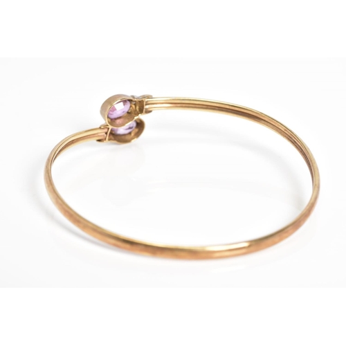 22 - A 9CT GOLD CROSSOVER BANGLE, the open bangle set with two oval cut amethyst and single cut diamond d... 