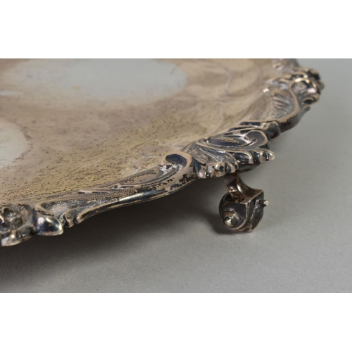 101 - AN EDWARDIAN SILVER CIRCULAR SALVER, cast foliate scroll rim, on three cabriole legs with scroll fee... 