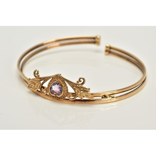 21 - A YELLOW METAL AMETHYST BANGLE, designed with a floral panel set with a heart cut amethyst, fitted t... 