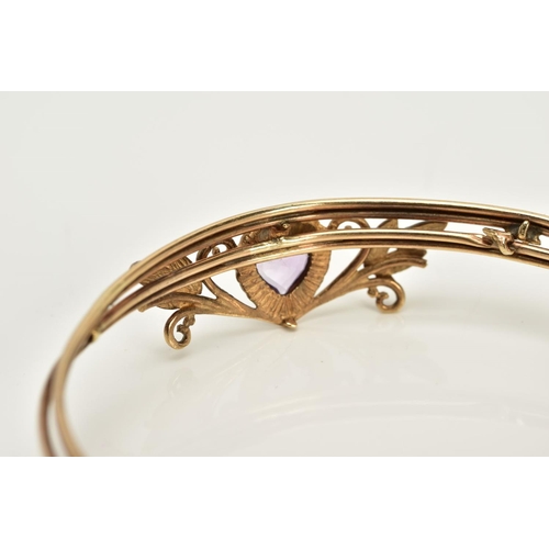 21 - A YELLOW METAL AMETHYST BANGLE, designed with a floral panel set with a heart cut amethyst, fitted t... 