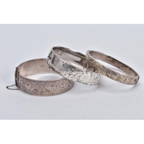 47 - THREE SILVER HINGED BANGLES, the first a wide bangle with a foliate engrave design, push pin clasp a... 