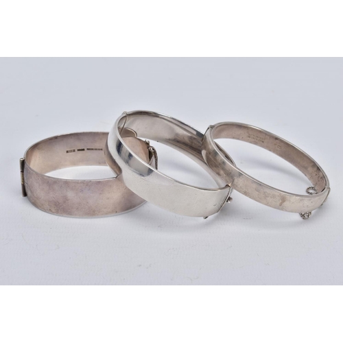 47 - THREE SILVER HINGED BANGLES, the first a wide bangle with a foliate engrave design, push pin clasp a... 