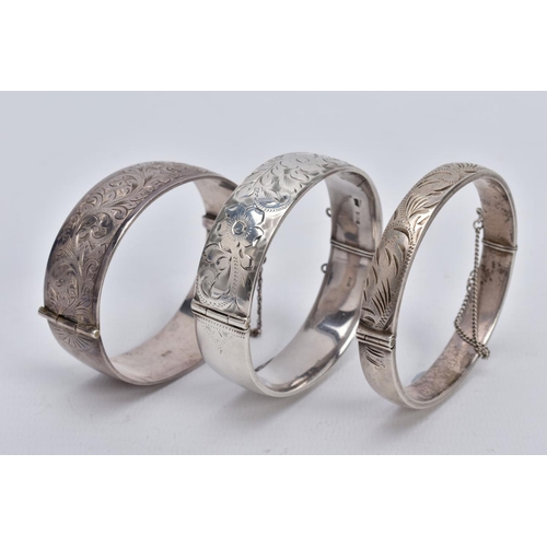 47 - THREE SILVER HINGED BANGLES, the first a wide bangle with a foliate engrave design, push pin clasp a... 