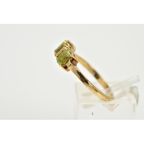 37 - A 9CT GOLD THREE STONE RING, designed with a row of three oval cut peridots, each interspaced with a... 