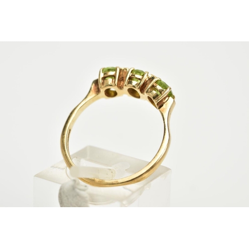 37 - A 9CT GOLD THREE STONE RING, designed with a row of three oval cut peridots, each interspaced with a... 