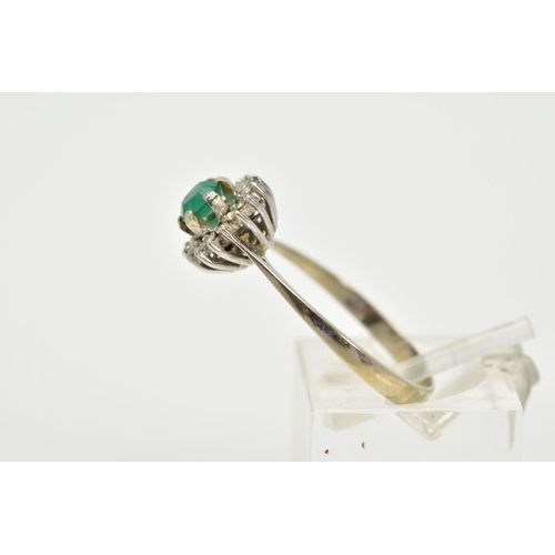 77 - A WHITE METAL EMERALD AND DIAMOND CLUSTER RING, designed with a central circular cut emerald within ... 