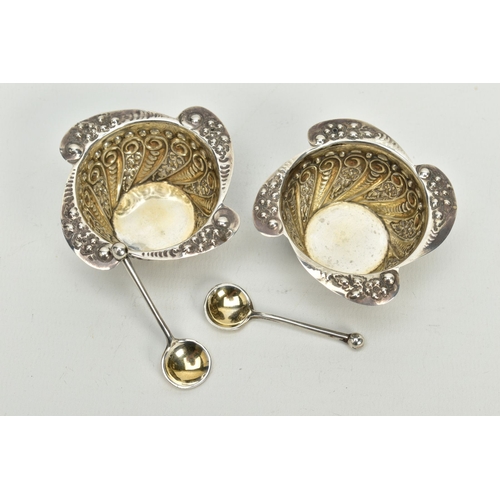 142 - A PAIR OF SILVER SALTS AND SPOONS, each salt with a scroll engraved body, wavy scroll detailed rim, ... 