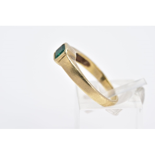 6 - A YELLOW METAL EMERALD RING, the emerald cut within a collet mount to the plain polished band, stamp... 