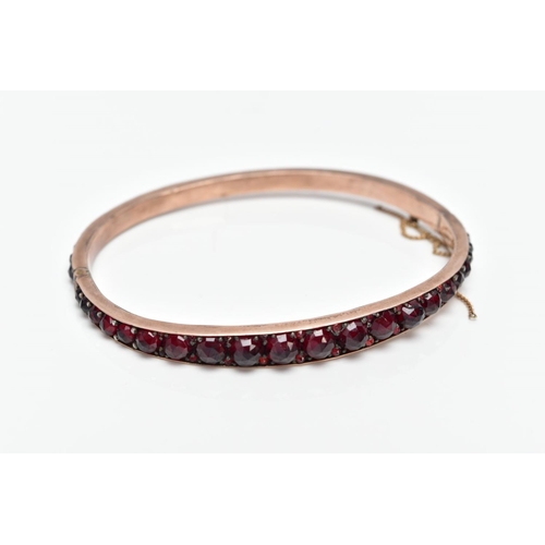 32 - A ROSE GOLD PLATED HINGED BANGLE, set with rose cut red and orange garnets all round, fitted with a ... 