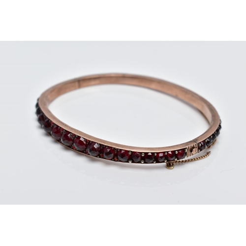 32 - A ROSE GOLD PLATED HINGED BANGLE, set with rose cut red and orange garnets all round, fitted with a ... 