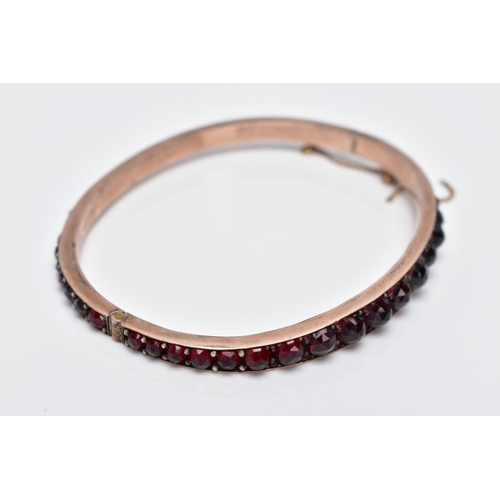 32 - A ROSE GOLD PLATED HINGED BANGLE, set with rose cut red and orange garnets all round, fitted with a ... 