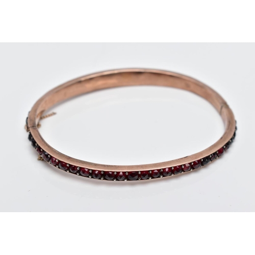 32 - A ROSE GOLD PLATED HINGED BANGLE, set with rose cut red and orange garnets all round, fitted with a ... 