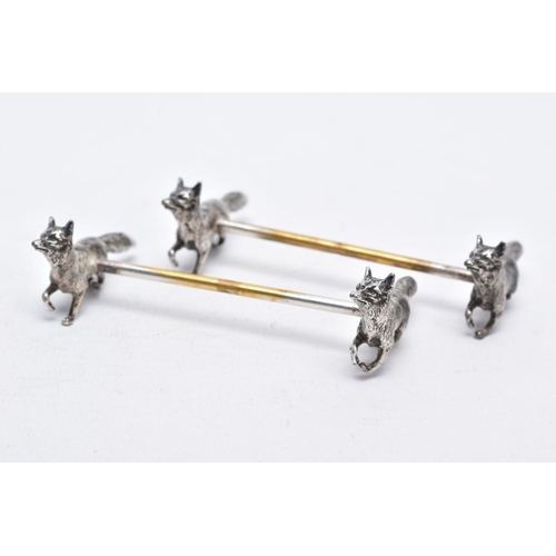 32 - A PAIR OF WHITE METAL KNIFE RESTS, each rest modelled with two foxes to each end with a worn gilt re... 