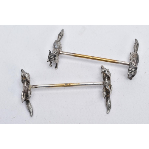 32 - A PAIR OF WHITE METAL KNIFE RESTS, each rest modelled with two foxes to each end with a worn gilt re... 