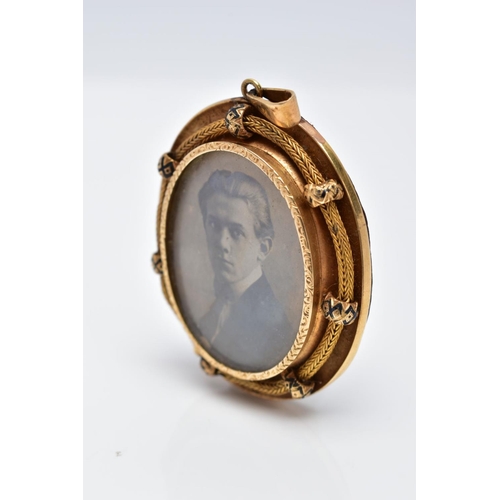 38 - A YELLOW METAL PORTRAIT PENDANT, of an oval form, holding a photo of a gentleman, within a textured ... 