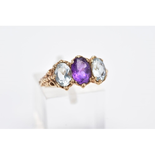 132 - A 9CT GOLD THREE STONE RING, centring on an oval cut amethyst, flanked with two oval cut aquamarines... 