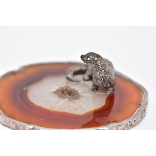 24 - A WHITE METAL OTTER ON AN AGATE AND SILVER MOUNTED BASE, textured figure of an otter fixed onto a ci... 