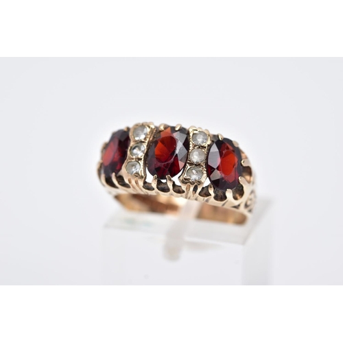 83 - A LATE 20TH CENTURY 9CT GOLD GARNET RING, designed with three oval cut garnets, interspaced with col... 