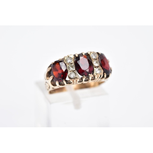 83 - A LATE 20TH CENTURY 9CT GOLD GARNET RING, designed with three oval cut garnets, interspaced with col... 