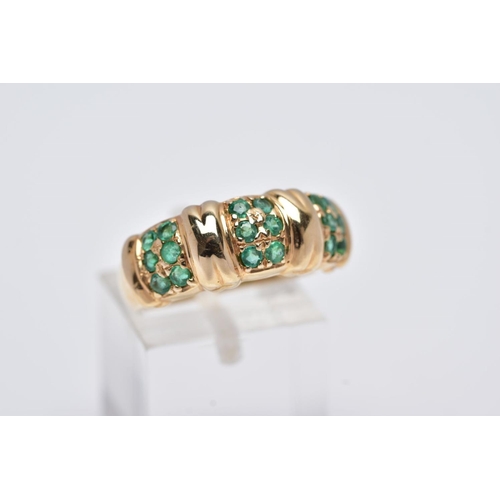 84 - A 14CT GOLD EMERALD RING, designed with three sections each set with two rows of circular cut emeral... 