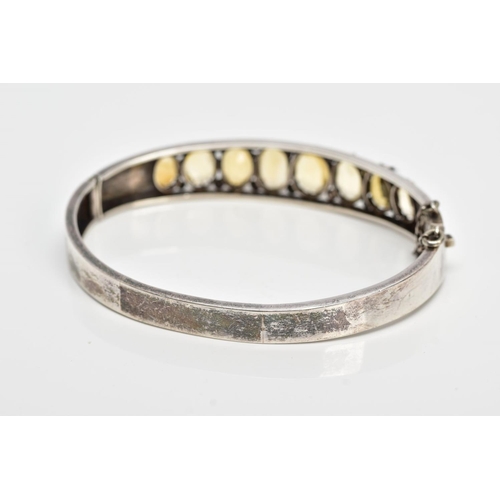 139 - A WHITE METAL CITRINE HINGED BANGLE, designed with a row of graduated claw set, oval cut citrines, o... 