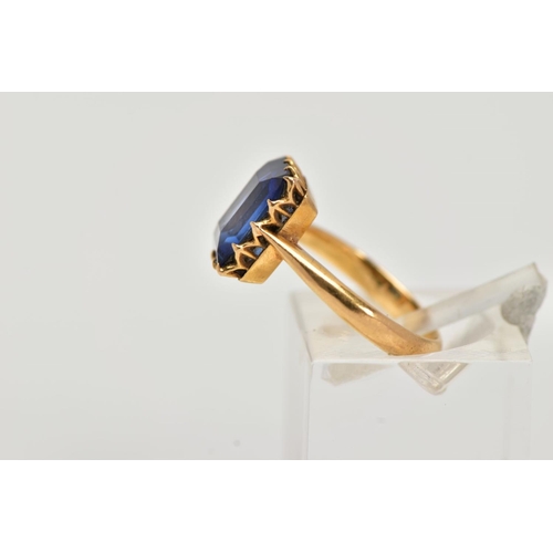 23 - A YELLOW METAL RING, designed with a claw set, rectangular cut synthetic blue sapphire, approximate ... 