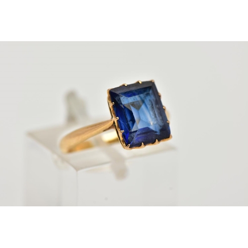 23 - A YELLOW METAL RING, designed with a claw set, rectangular cut synthetic blue sapphire, approximate ... 