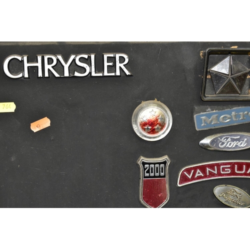 764 - CAR BADGES AND WHEEL TRIMS, a collection of car badges attached to a wooden frame to include Austin,... 