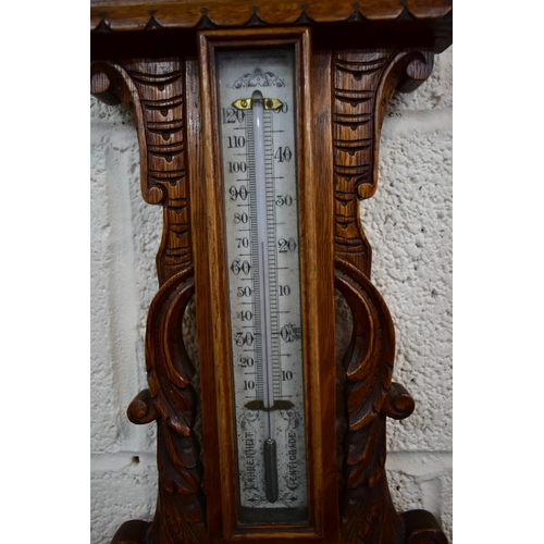 85A - A LATE VICTORIAN CARVED OAK ANEROID BAROMETER, with mercury thermometer and working blued indicator,... 