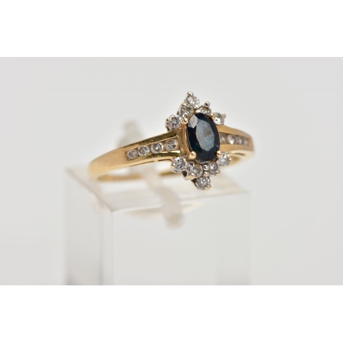 16 - AN 18CT GOLD SAPPHIRE AND DIAMOND CLUSTER RING, centring on an oval cut blue sapphire, within a roun... 