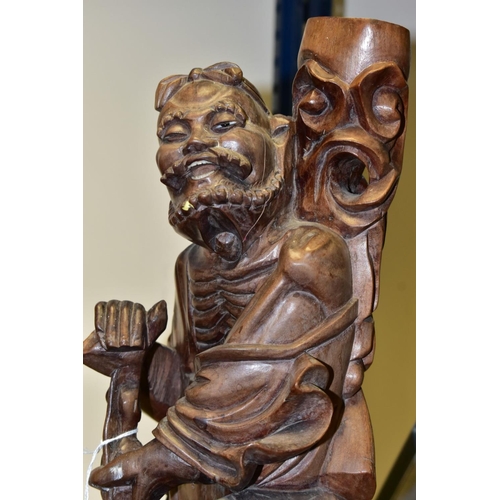 323 - A 20TH CENTURY CHINESE CARVED HARDWOOD FIGURE OF A JOVIAL MAN, holding a staff in both hands, a styl... 