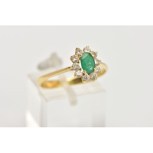 32 - A YELLOW METAL EMERALD AND CUBIC ZIRCONIA CLUSTER RING, centring on a claw set, oval cut emerald, wi... 