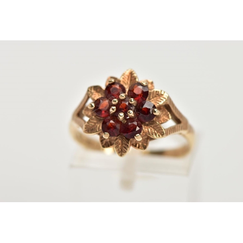 37 - A 9CT GOLD GARNET DRESS RING, of a flower shape, set with seven circular cut garnets, textured leaf ... 