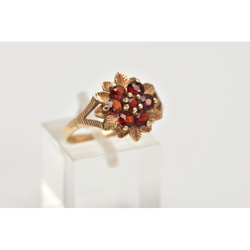 37 - A 9CT GOLD GARNET DRESS RING, of a flower shape, set with seven circular cut garnets, textured leaf ... 