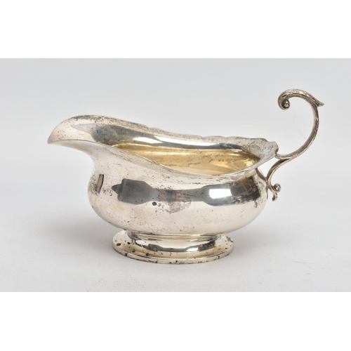 53 - A GEORGE V SILVER SAUCE BOAT, plain polished body, wavy detailed rim, scroll and leaf detailed handl... 