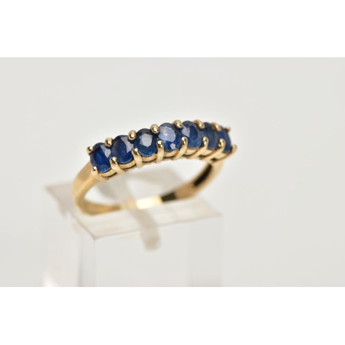 12 - A 9CT GOLD SAPPHIRE DRESS RING, of a half hoop design, set with a row seven claw set, oval cut, blue... 