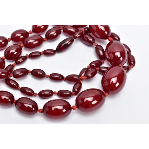 31 - A CHERRY AMBER STYLE BAKELITE BEAD NECKLACE, graduated oval beads individually knotted on a red cord... 