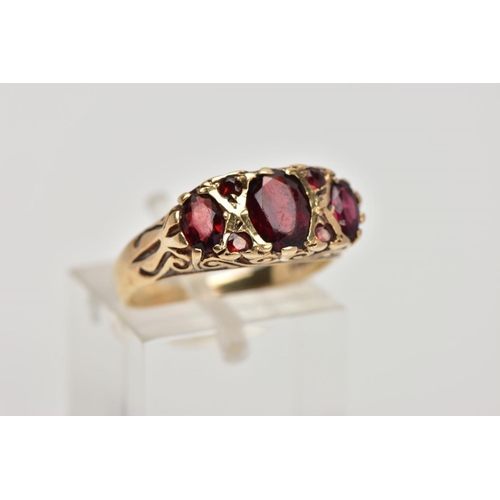 268 - A 9CT GOLD THREE STONE GARNET RING, designed with a row of three graduated oval cut garnets, intersp... 