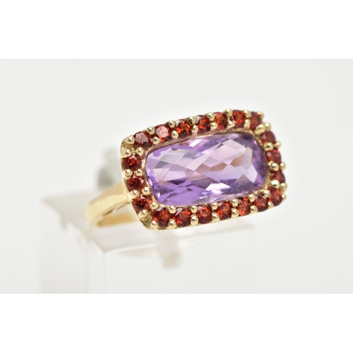 29 - AN AMETHYST AND GARNET DRESS RING, a fancy cut amethyst set with a halo of circular cut garnet stone... 