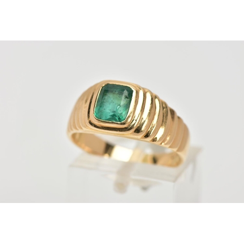 59 - A YELLOW METAL EMERALD SIGNET RING, centring on an emerald cut emerald, bezel set, textured design e... 