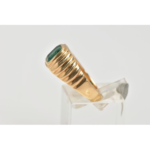 59 - A YELLOW METAL EMERALD SIGNET RING, centring on an emerald cut emerald, bezel set, textured design e... 