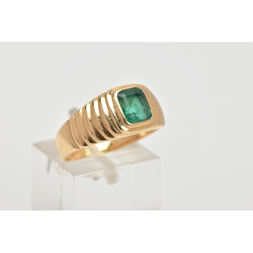 59 - A YELLOW METAL EMERALD SIGNET RING, centring on an emerald cut emerald, bezel set, textured design e... 