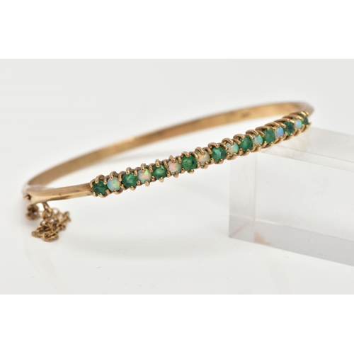 60 - A 9CT GOLD EMERALD AND OPAL BANGLE, hinged bangle, designed with a row of circular cut emeralds inte... 